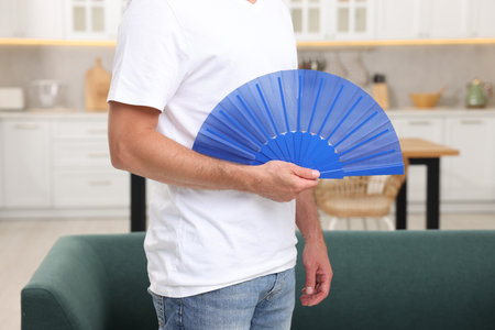 Man with blue hand fan in kitchen, closeupの写真素材