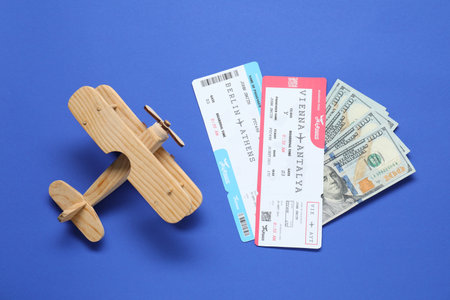 Dollars, wooden model of plane and tickets on blue table, flat lay. Business tripの写真素材