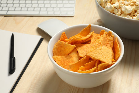 Bad eating habits at workplace. Tasty tortilla chips in bowl on wooden table, closeupの写真素材