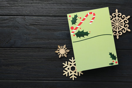 Blank Christmas invitation card and decorative snowflakes on black wooden table, flat lay. Space for textの写真素材