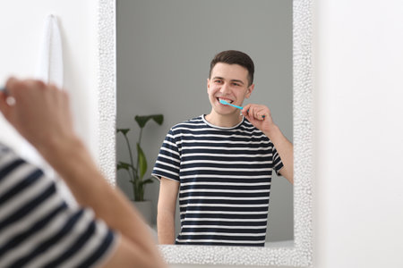 Man brushing his teeth with toothbrush near mirror in bathroomの写真素材