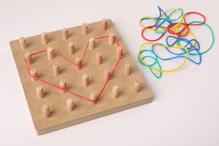 Wooden geoboard with heart made of rubber bands on white table. Educational toy for motor skills developmentの写真素材