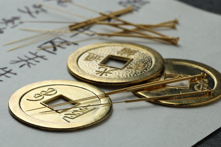 Acupuncture needles, ancient coins and paper with characters on table, closeup