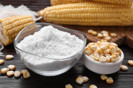 Bowl with corn starch and kernels on dark wooden table, closeup