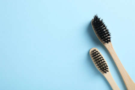 Two bamboo toothbrushes on light blue background, flat lay. Space for text