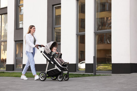 Beautiful nanny with cute little boy in stroller walking outdoors