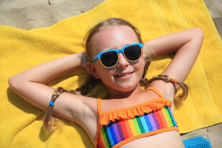 Happy little girl in sunglasses enjoying sunny day on sandy beachの写真素材