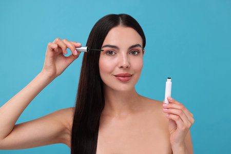 Beautiful woman applying serum onto her eyelashes on light blue background. Cosmetic product