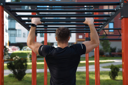 Man training on monkey bars at outdoor gym, back view
