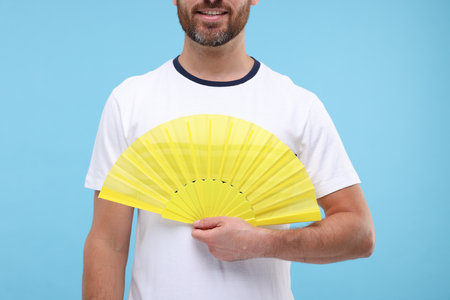 Man holding hand fan on light blue background, closeupの写真素材