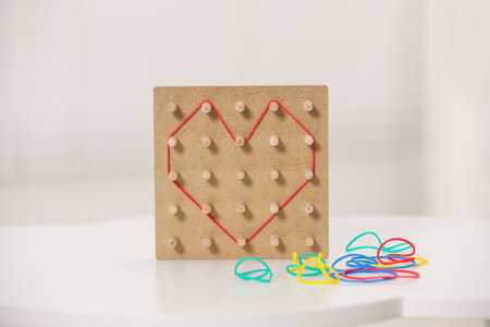 Wooden geoboard with rubber bands on white table indoors. Educational toy for motor skills developmentの写真素材