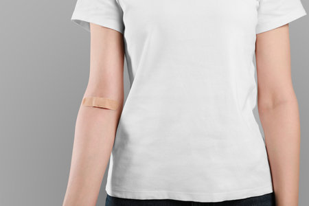 Blood donation concept. Woman with adhesive plaster on arm against gray background, closeup