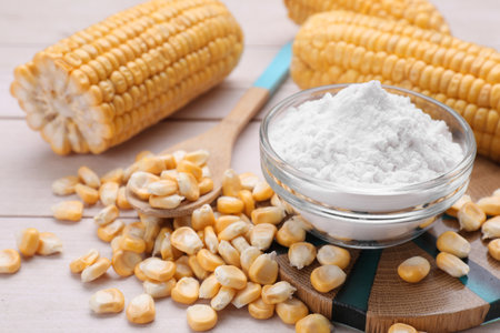 Bowl with corn starch, ripe cobs and kernels on wooden tableの写真素材