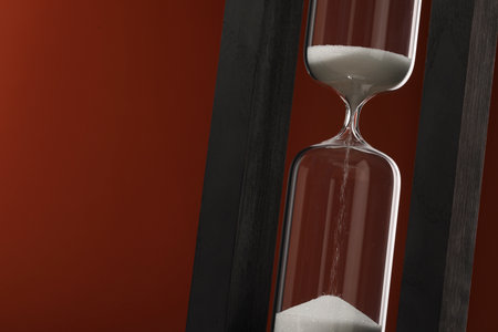 Hourglass with flowing sand on brown background, closeup. Space for text