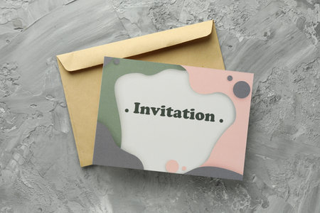 Beautiful card with word Invitation and envelope on gray table, flat lay