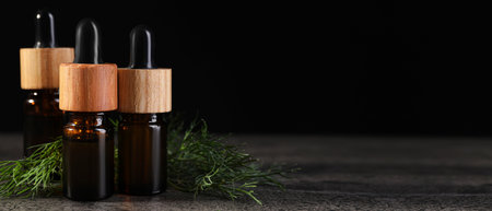 Bottles of dill essential oil on wooden table against black background. Banner design with space for textの写真素材