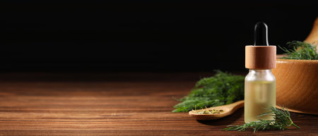 Bottle of dill essential oil on wooden table against black background. Banner design with space for textの写真素材