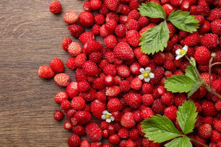 Many fresh wild strawberries, flowers and leaves on wooden table, flat lay. Space for textの写真素材
