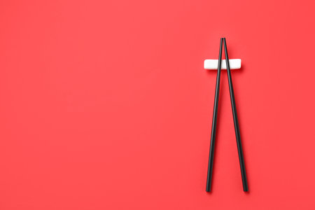 Pair of black chopsticks with rest on red background, top view. Space for textの写真素材