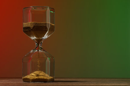 Hourglass with flowing sand on wooden table against color background, space for textの写真素材