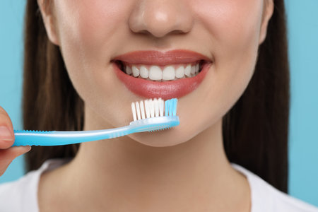 Woman brushing her teeth with plastic toothbrush on light blue background, closeupの写真素材