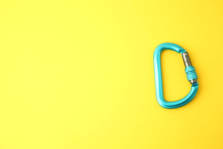 One light blue carabiner on yellow background, top view. Space for textの写真素材