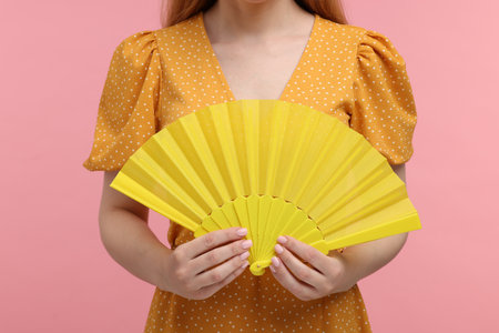 Woman with yellow hand fan on pink background, closeupの写真素材