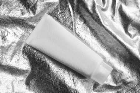 Tube with face cleansing product on silver background, top view
