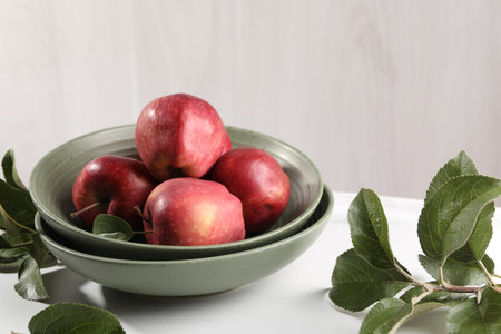 Fresh red apples and leaves on white table