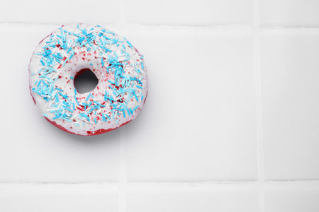 Glazed donut decorated with sprinkles on white tiled table, top view. Space for text. Tasty confectioneryの写真素材