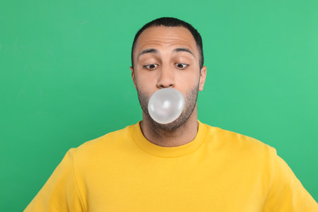 Portrait of young man blowing bubble gum on green backgroundの写真素材