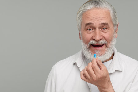 Senior man taking pill on grey background. Space for text