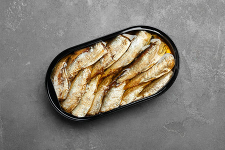 Canned sprats on gray textured table, top view