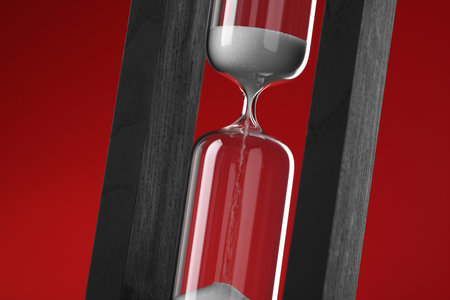 Hourglass with flowing sand on red background, closeup