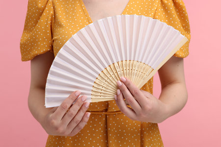 Woman with hand fan on pink background, closeupの写真素材