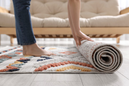 Woman unrolling carpet with beautiful pattern on floor in room, closeupの写真素材