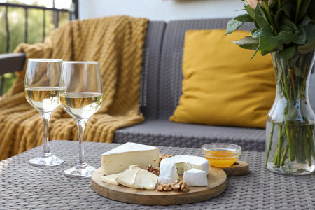 Vase with roses, glasses of wine and snacks on rattan table at balcony