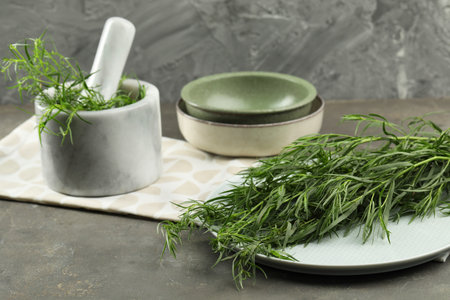 Plate and mortar with fresh tarragon leaves on gray tableの写真素材
