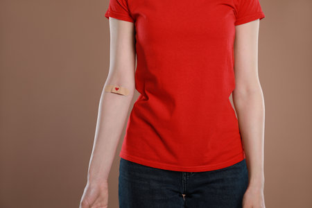 Blood donation concept. Woman with adhesive plaster on arm against brown background, closeup. Space...