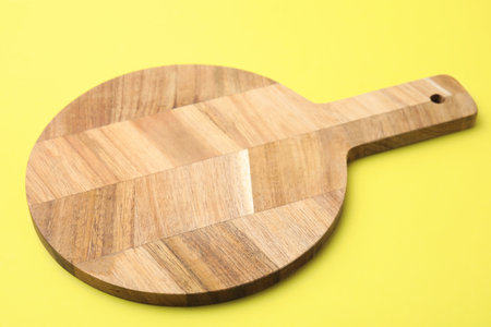 One wooden cutting board on yellow background, closeup. Cooking utensilの写真素材