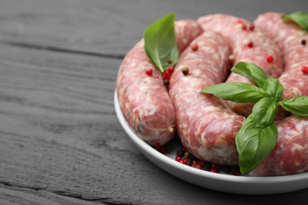 Raw homemade sausages, basil leaves and peppercorns on gray wooden table, closeup. space for textの写真素材