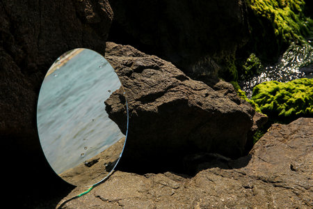 Round mirror reflecting sea on stones outdoorsの写真素材