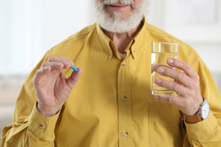 Senior man with glass of water and pill indoors, closeupの写真素材