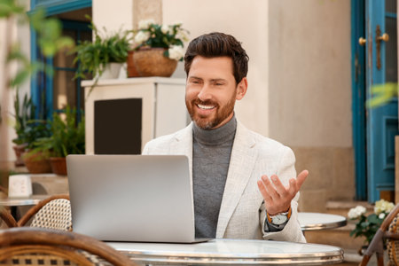 Man having video chat via laptop at table in outdoor cafe