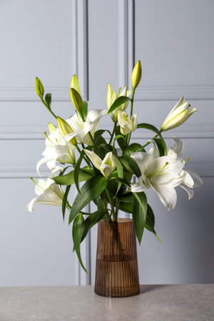 Beautiful bouquet of lily flowers in glass vase on light gray tableの写真素材