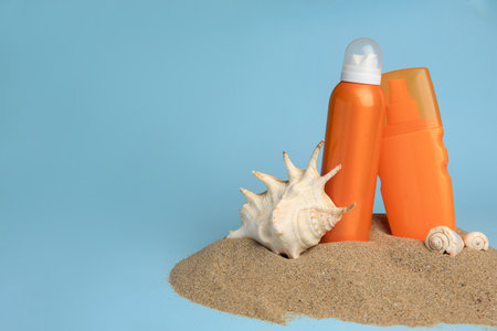 Sand with bottles of sunscreens and seashells against light blue background, space for text. Sun...