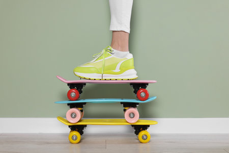 Woman in new stylish sneaker standing on skateboards near light green wall, closeup