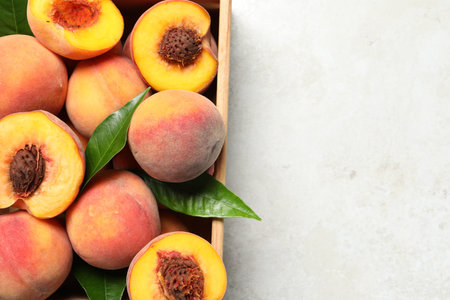 Delicious juicy peaches and leaves in crate on light gray textured table, top view. Space for textの写真素材
