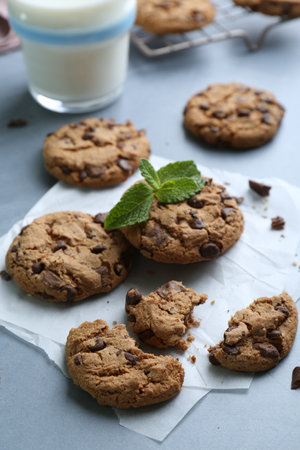 Tasty chocolate chip cookies, glass of milk and mint leaves on light gray table