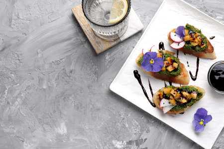 Delicious bruschettas with pesto sauce, tomatoes and balsamic vinegar served on gray textured table,...